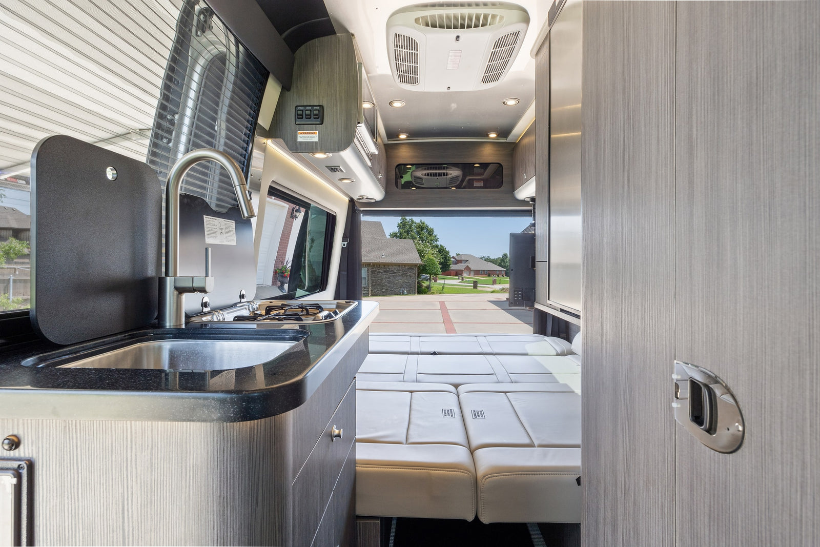 parked on a driveway on a sunny day.|Rear view of a silver Mercedes-Benz Airstream Interstate RV