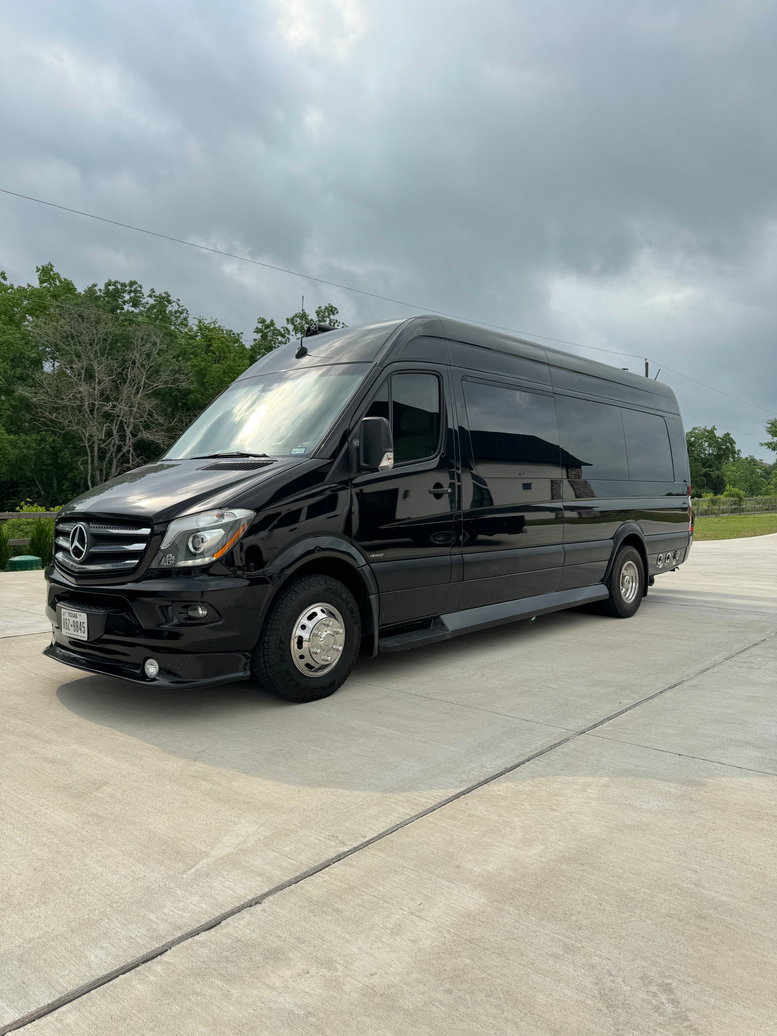 Black Mercedes-Benz Sprinter luxury RV rental van parked on concrete under an overcast sky.