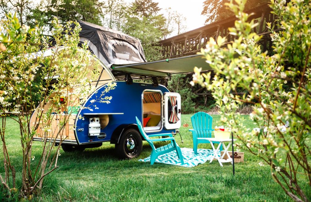 and colorful striped accents.|Vibrant blue teardrop RV rental features a rooftop tent