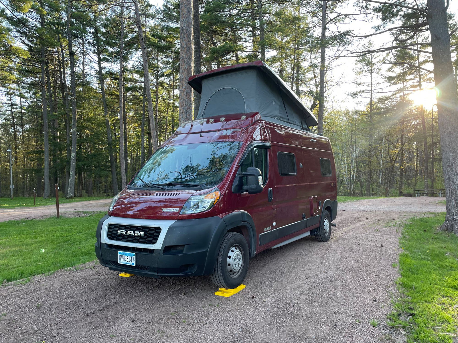 pop-top extended for adventure.|This RV rental in a serene wooded campsite features a red pop-top camper van ready for adventure.|Maroon RV rental with two bikes and a pop-top roof