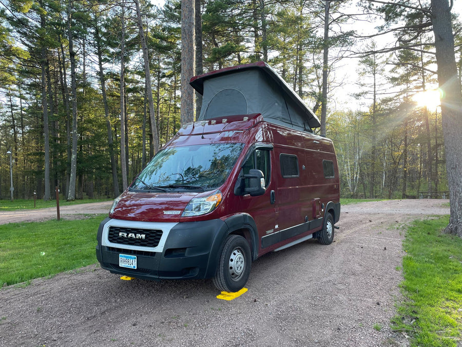 pop-top extended for adventure.|This RV rental in a serene wooded campsite features a red pop-top camper van ready for adventure.|Maroon RV rental with two bikes and a pop-top roof