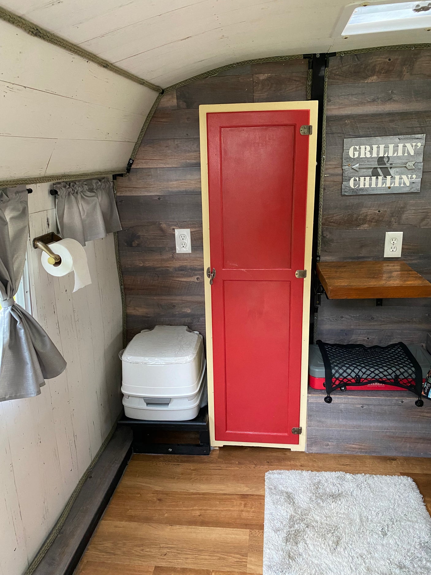 Inside an RV rental: a compact living space with a portable toilet, rustic wood finishes, and a vibrant red cabinet door.