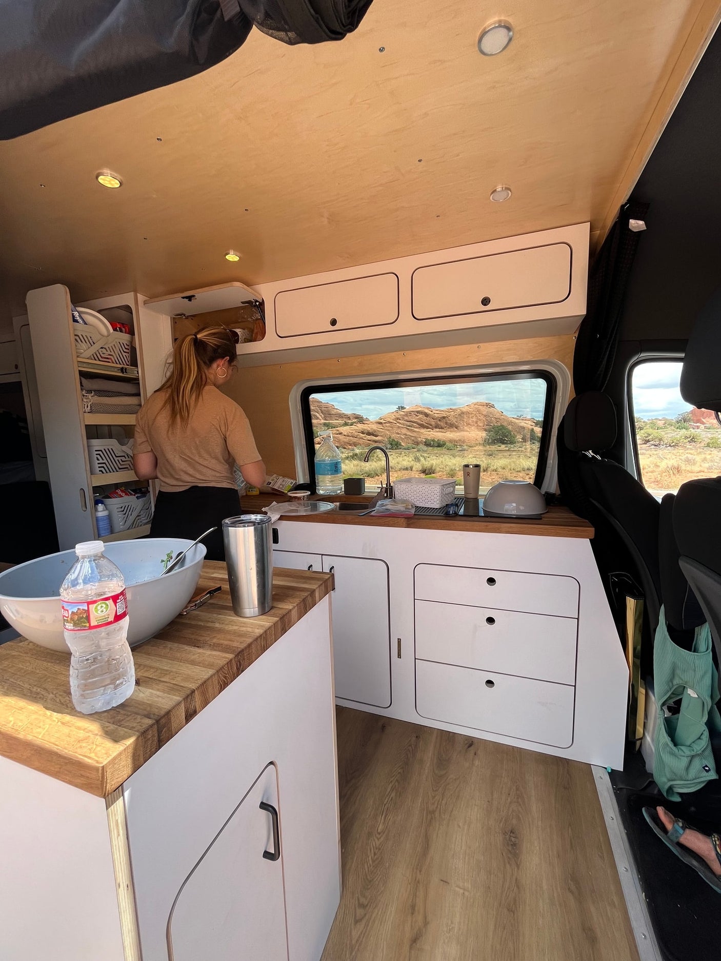 Woman cooking in a well-equipped RV rental kitchen. Camper van interior with wood countertops & a scenic desert view.