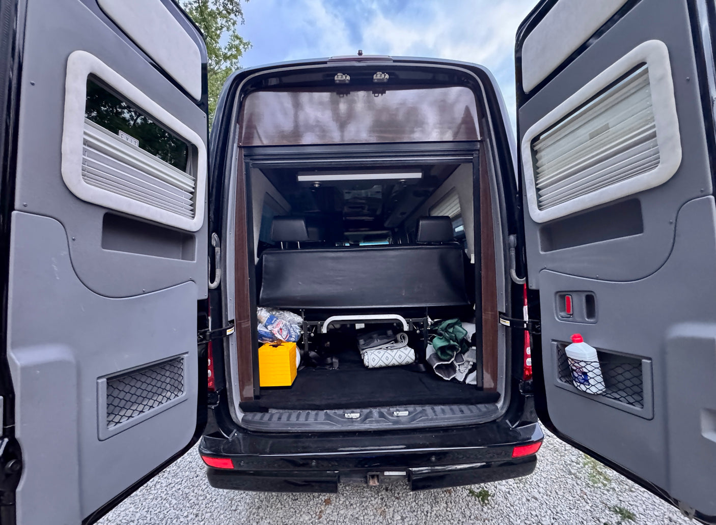 Rear of an RV rental with open doors revealing interior storage, a yellow box, and a white bottle in a door pocket.
