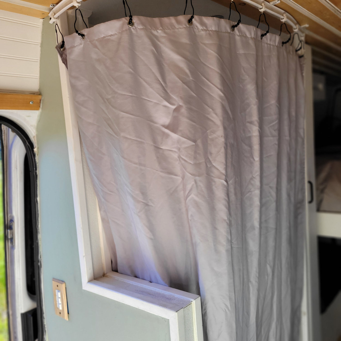 RV rental: Light-colored privacy curtain on track inside a camper van, with wall-mounted switch visible.