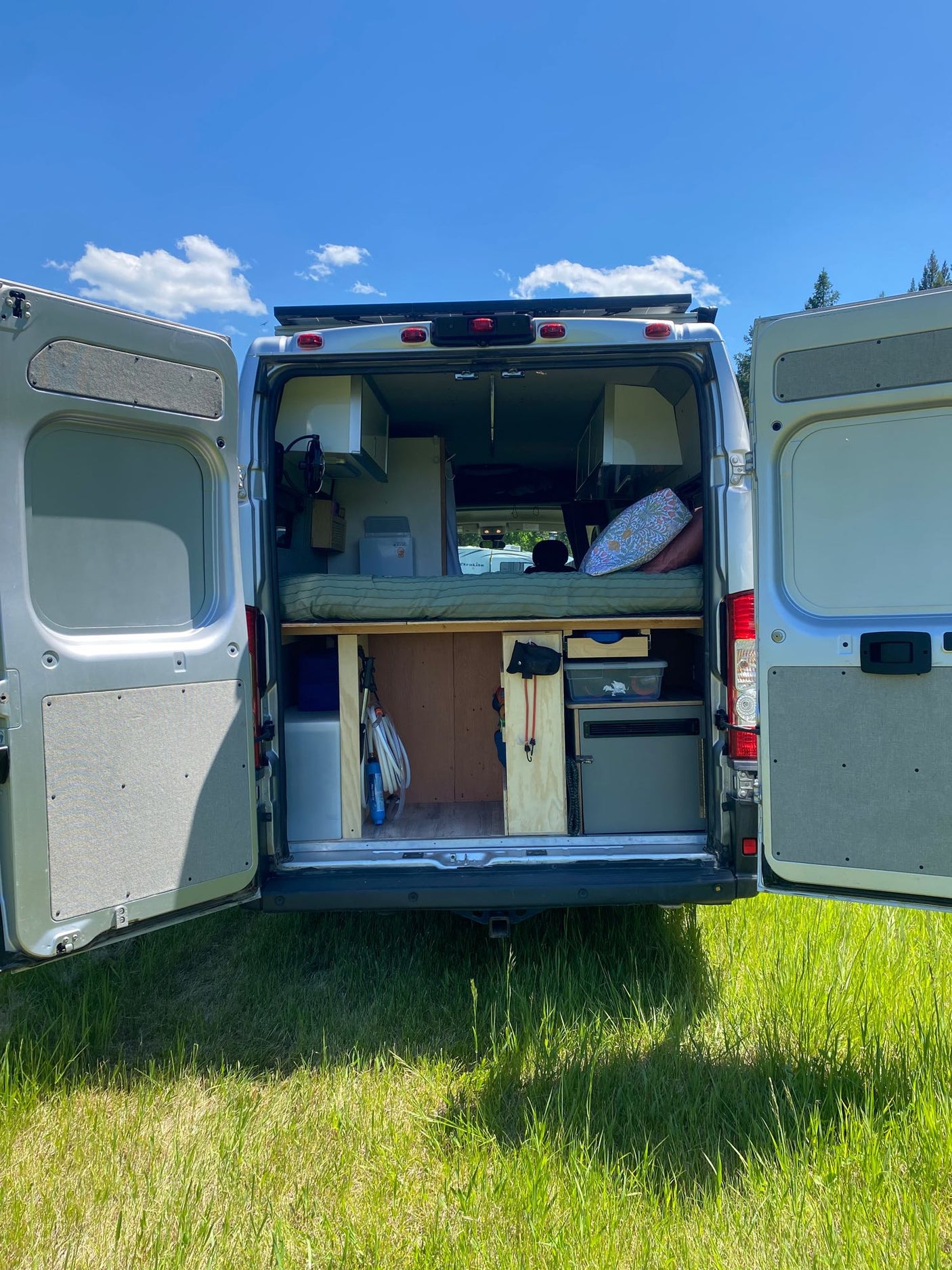 This RV rental campervan's open rear doors reveal a bed & organized storage, perfect for your next outdoor adventure in nature.