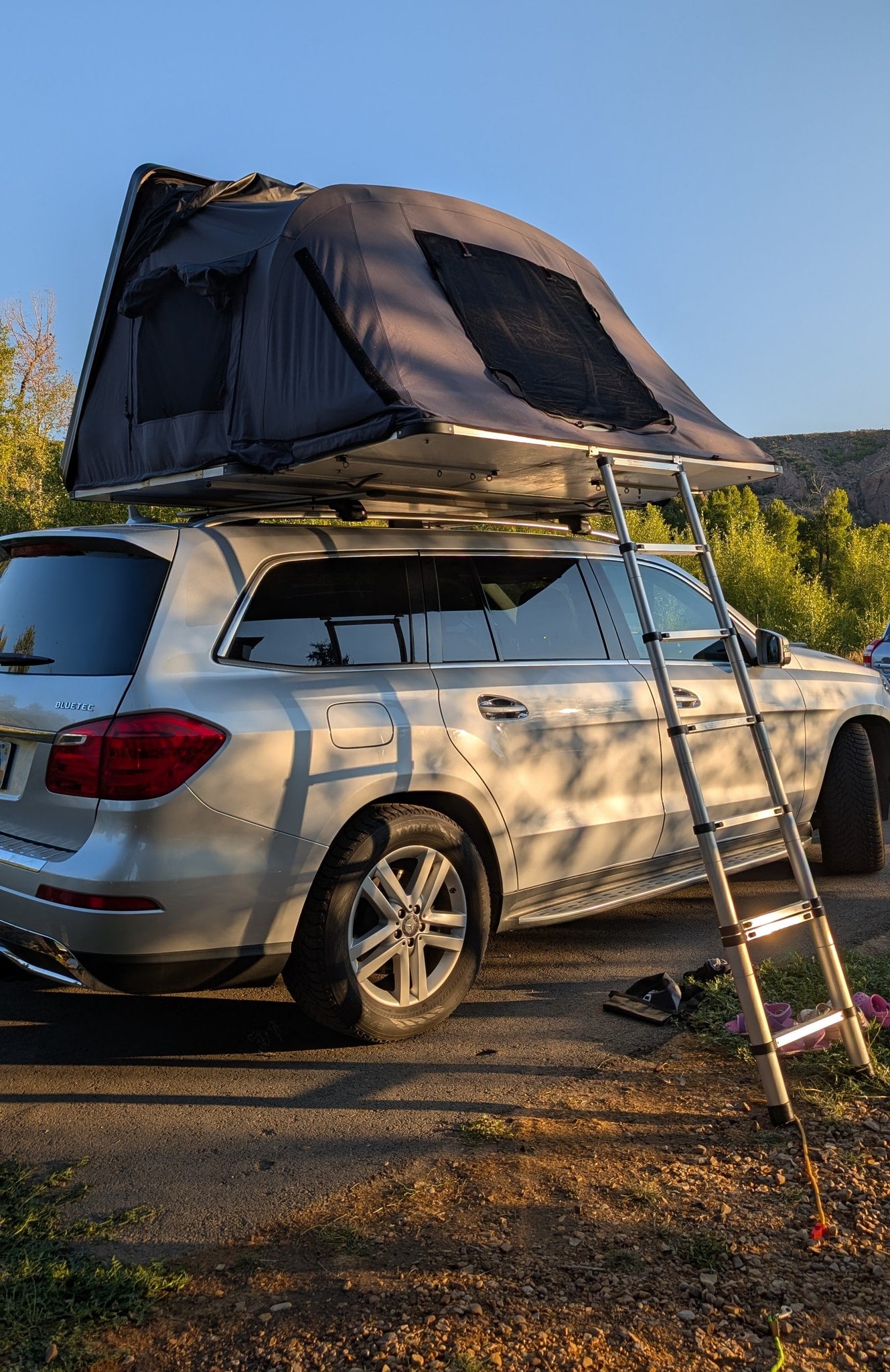 Compact RV rental: a silver Mercedes SUV with a deployed rooftop tent and ladder, perfect for outdoor camping.