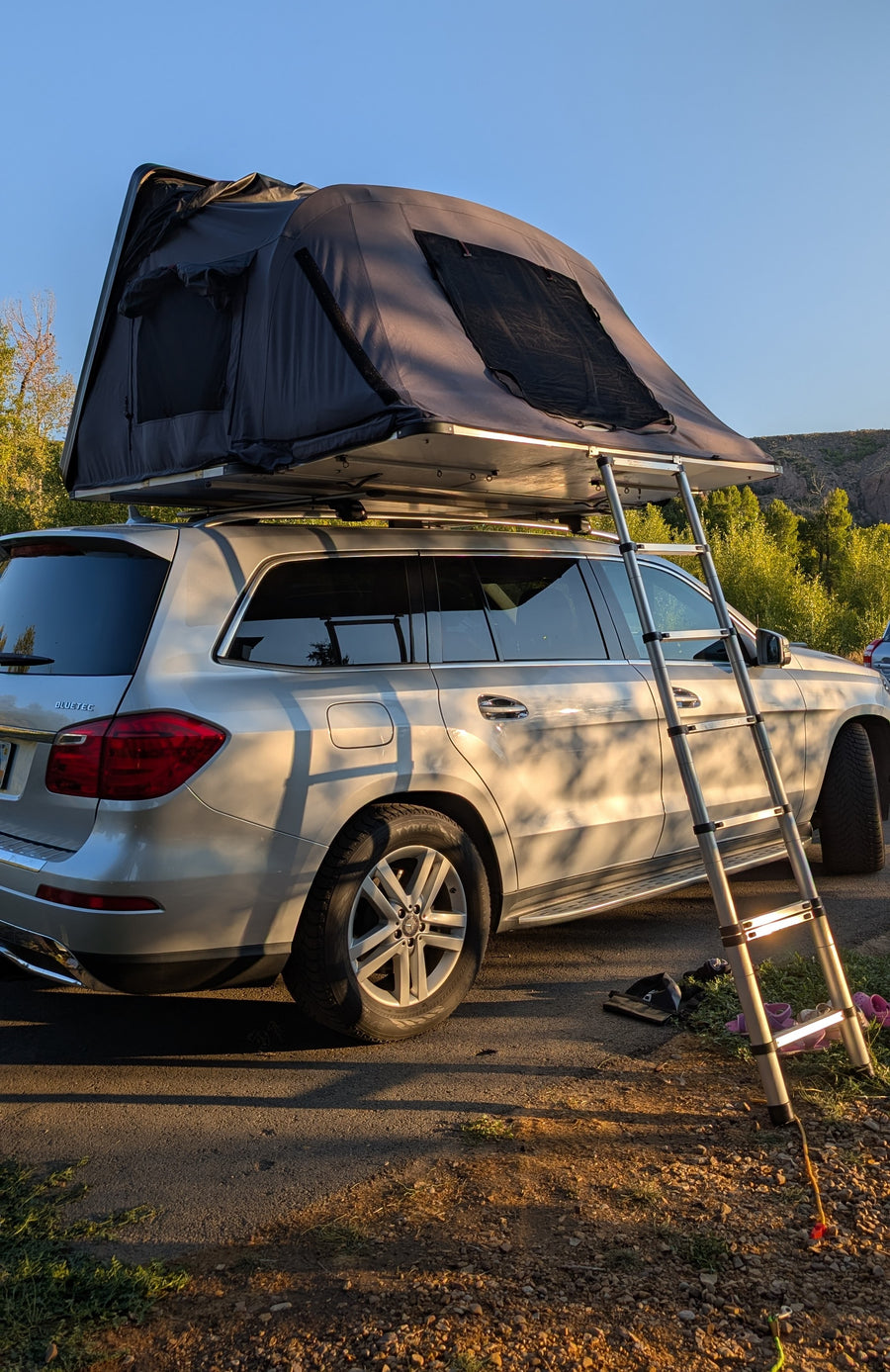 Compact RV rental: a silver Mercedes SUV with a deployed rooftop tent and ladder, perfect for outdoor camping.
