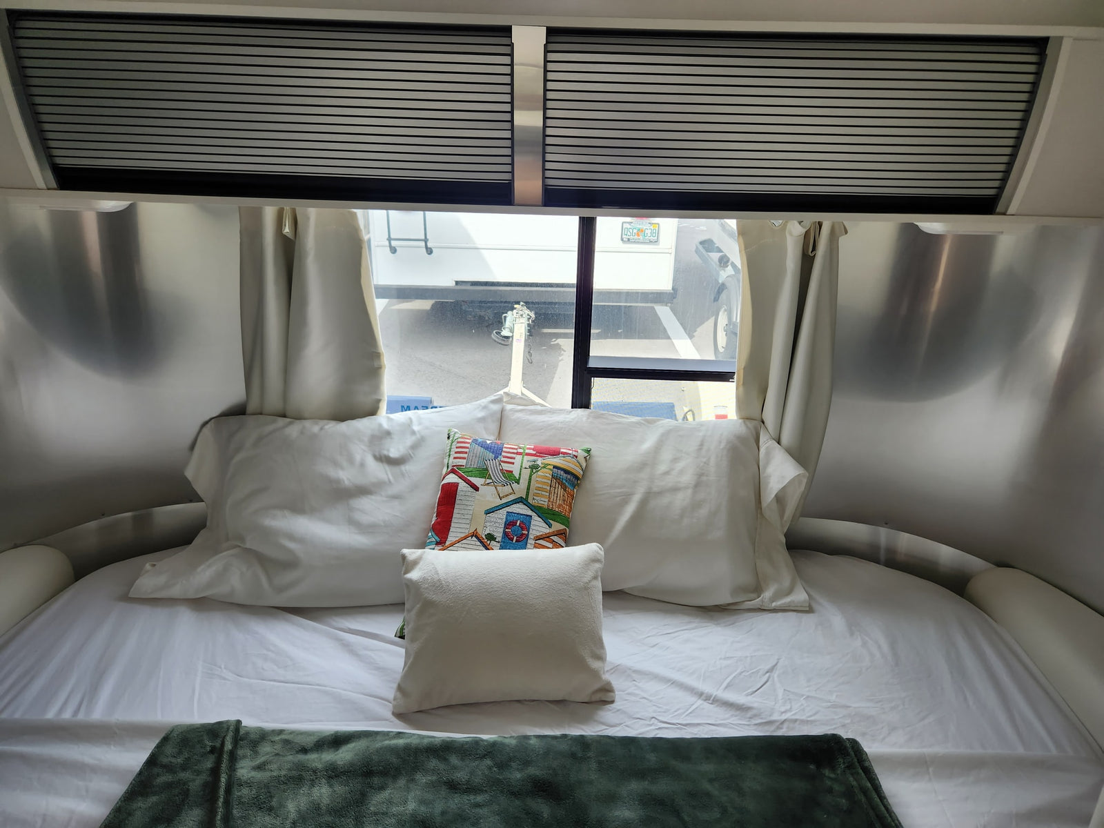 Inside a comfortable rv rental: a cozy bedroom with a white bed, colorful pillow, and window views.