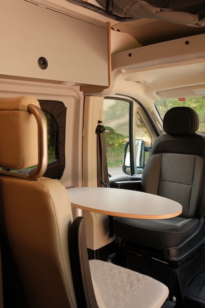 RV rental interior with a table between front swivel seats and overhead storage. Ideal for travel comfort.