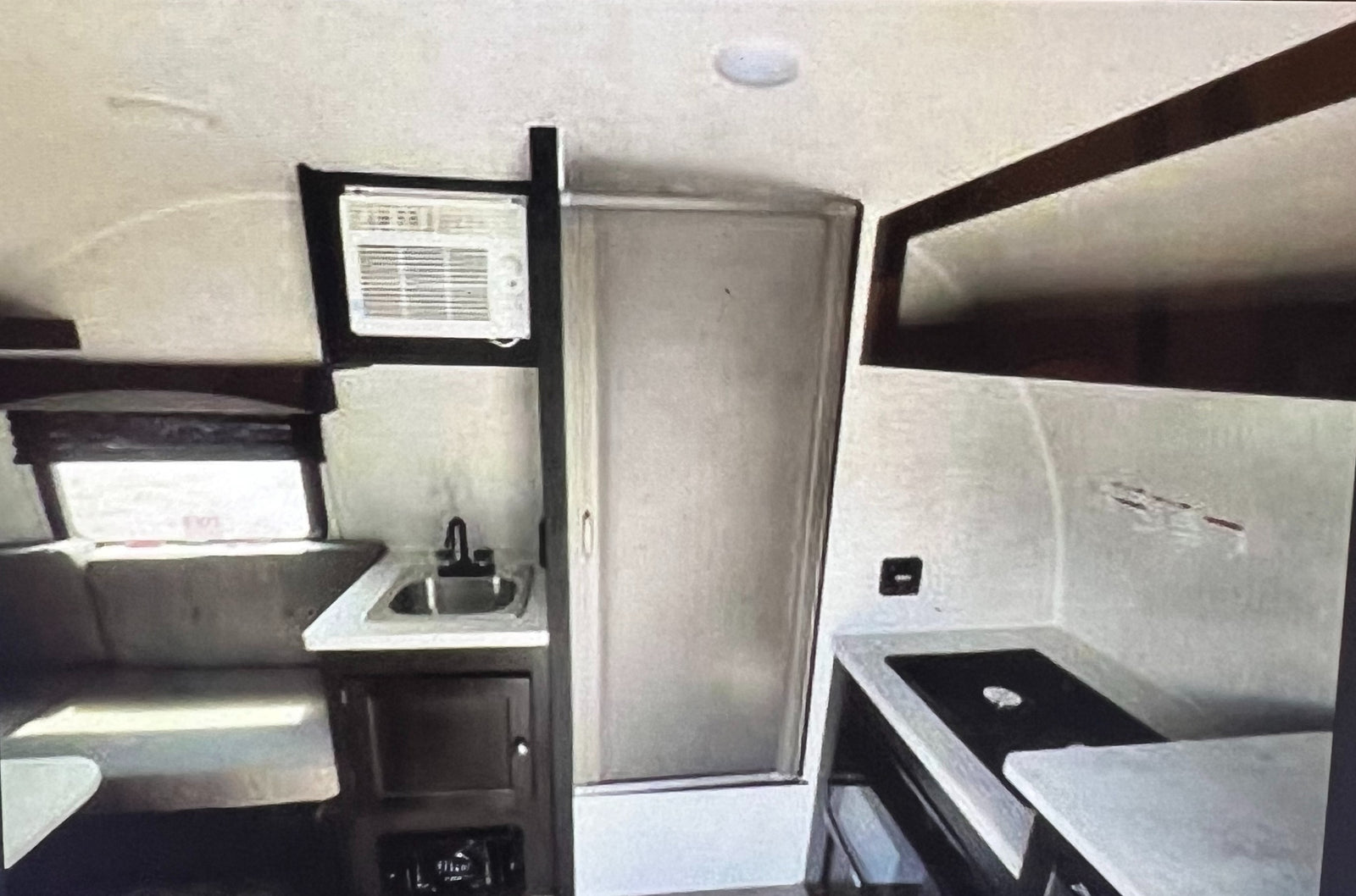 RV rental: Inside view of a compact camper kitchen with sink, window AC, dinette, and bathroom door.