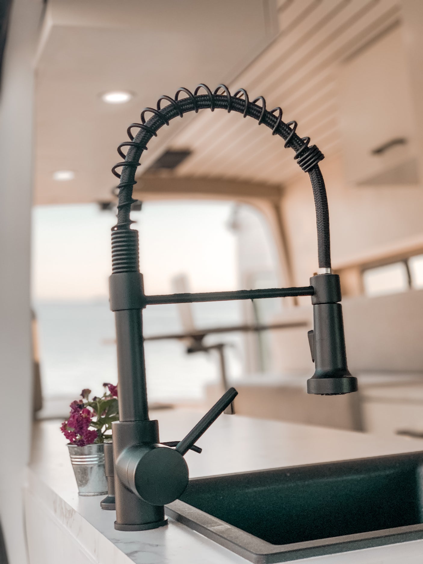 Modern RV rental kitchen with a black gooseneck faucet, sink, and marble-look countertop, featuring purple flowers.