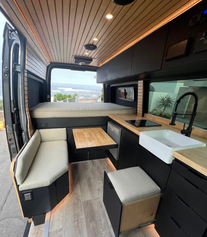 Step inside this custom RV rental camper van! A modern interior with wood accents, kitchen, bed, dining, and ocean view awaits.