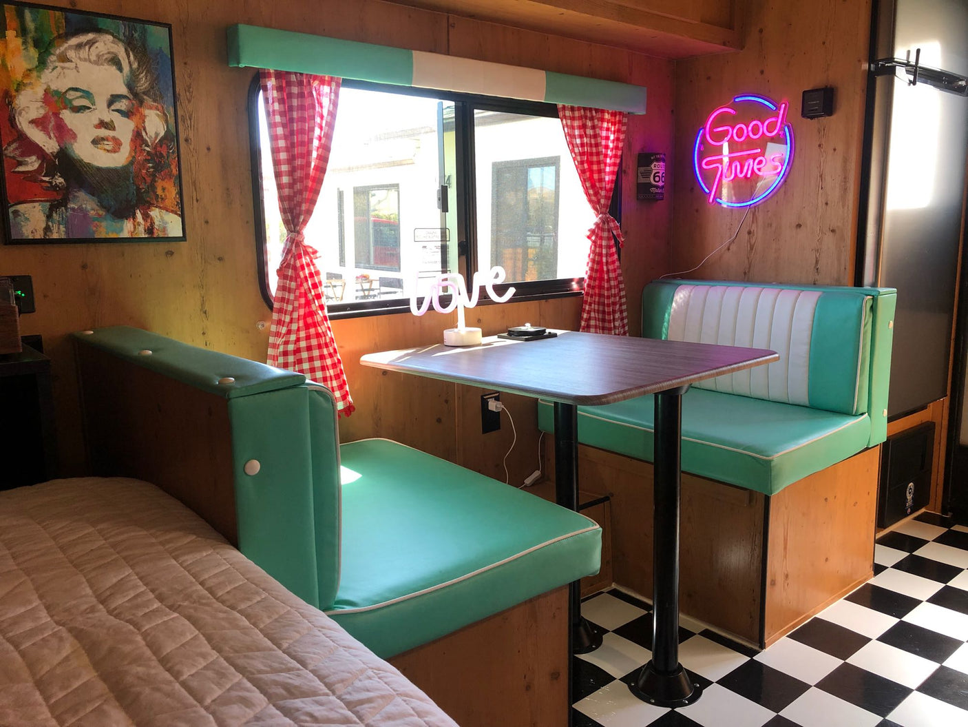 Explore this retro RV rental's vibrant interior: a teal diner booth, checkered floor, Marilyn Monroe pop art, & neon signs.