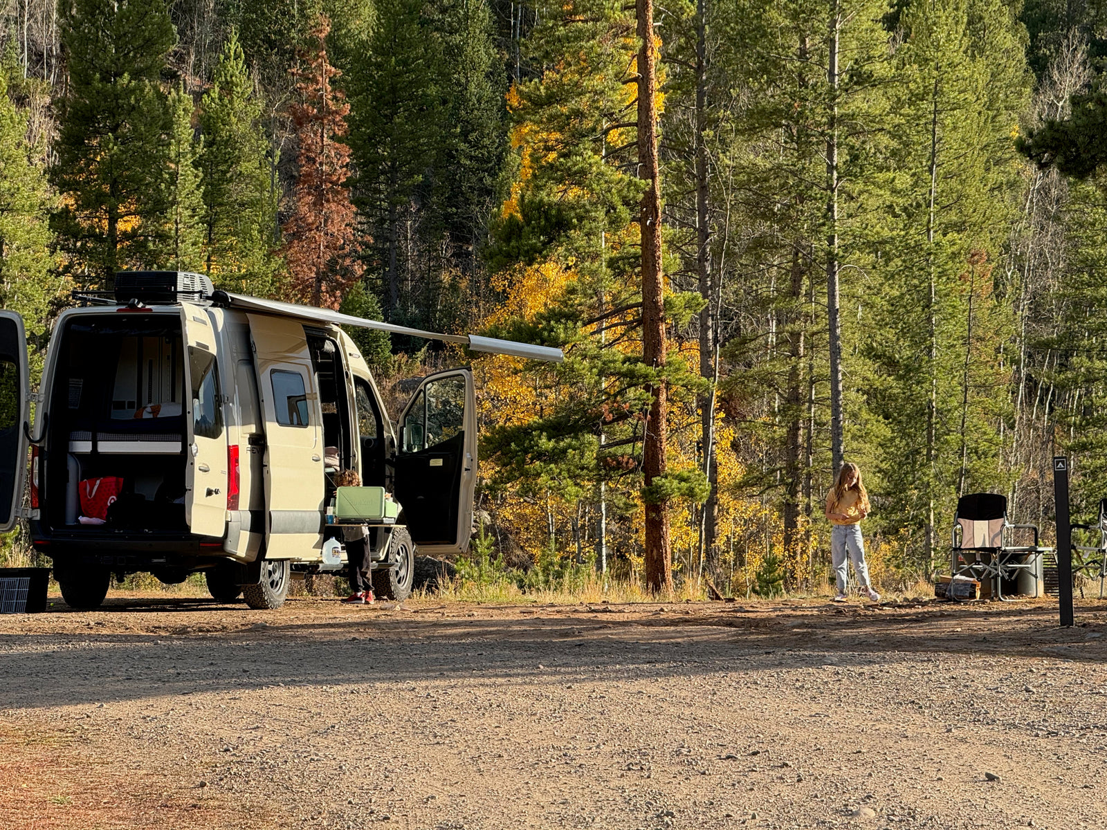 A person stands by their RV rental camper van in a vibrant fall forest campsite.