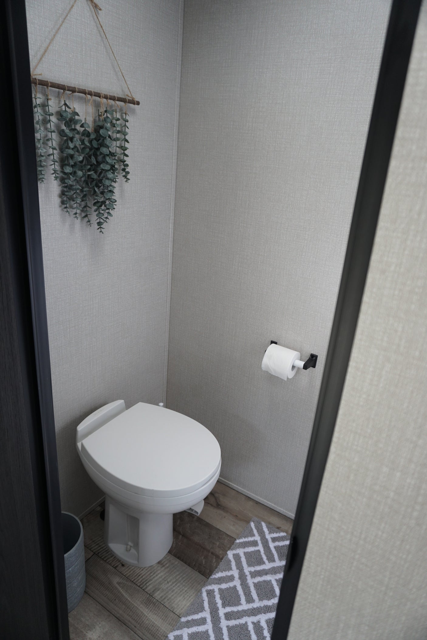 This RV rental's compact bathroom features a white toilet, eucalyptus decor, textured walls, and a geometric bath mat.