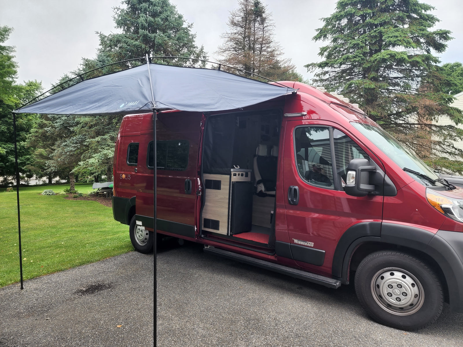 A red Winnebago Solis camper van with extended awning & open side door, showcasing interior. Ideal for rv rental.