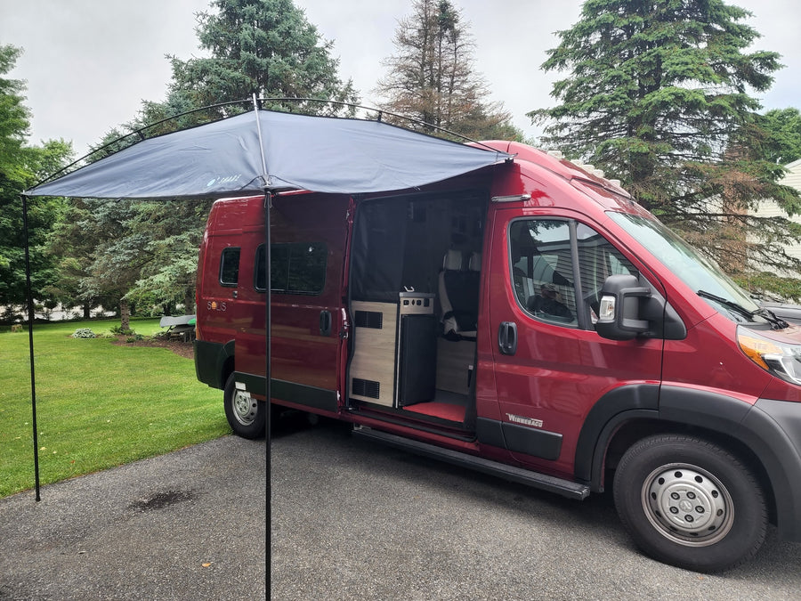 A red Winnebago Solis camper van with extended awning & open side door, showcasing interior. Ideal for rv rental.