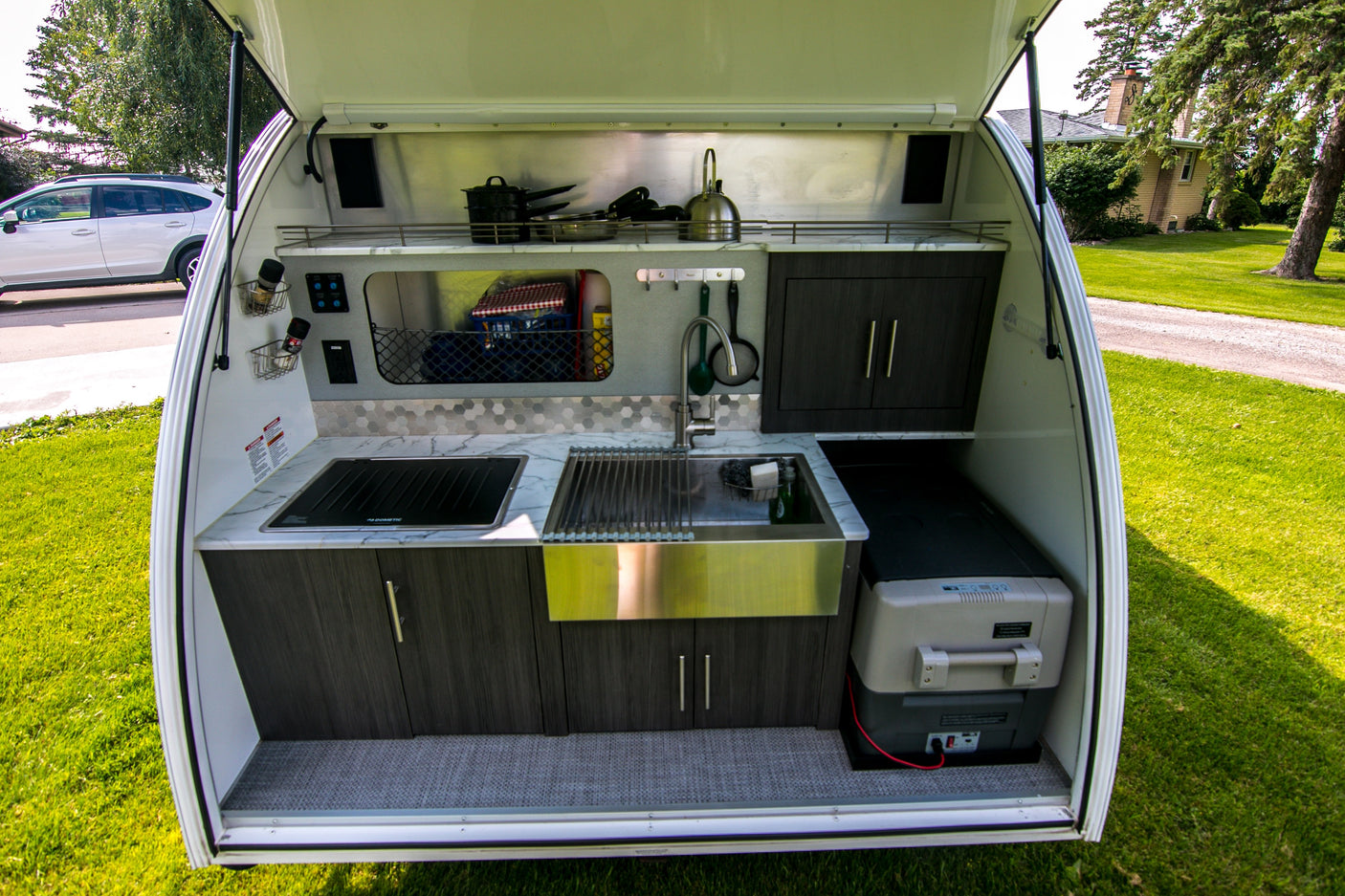 Rear kitchen in a compact RV rental, featuring a sink, stovetop, cabinets, and portable cooler for outdoor cooking.