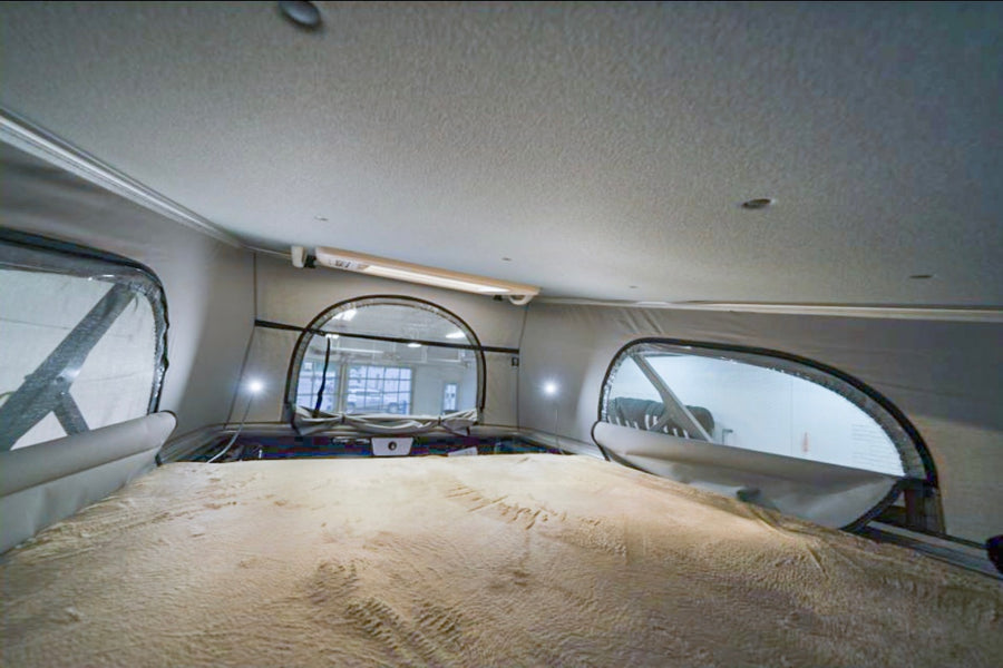 Spacious pop-top RV rental interior with a cozy bed, perfect for your next road trip adventure. Features large windows.