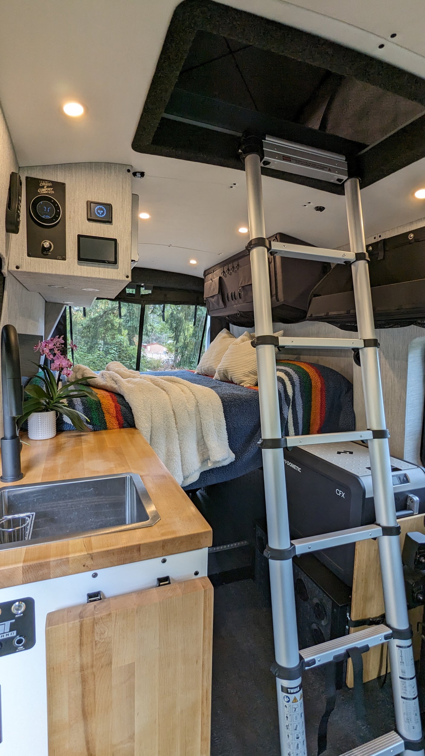 Inside a sleek rv rental: Compact kitchen, cozy bed, ladder to versatile overhead space, and Dometic cooler.