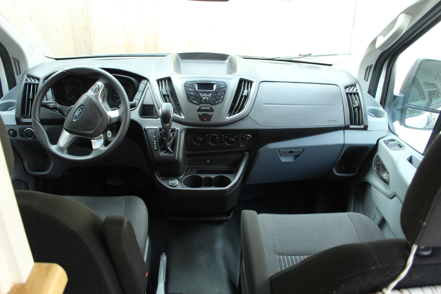 Inside a Ford Transit van, ideal for RV rental. View of the dashboard, steering wheel, and front cockpit from the rear.