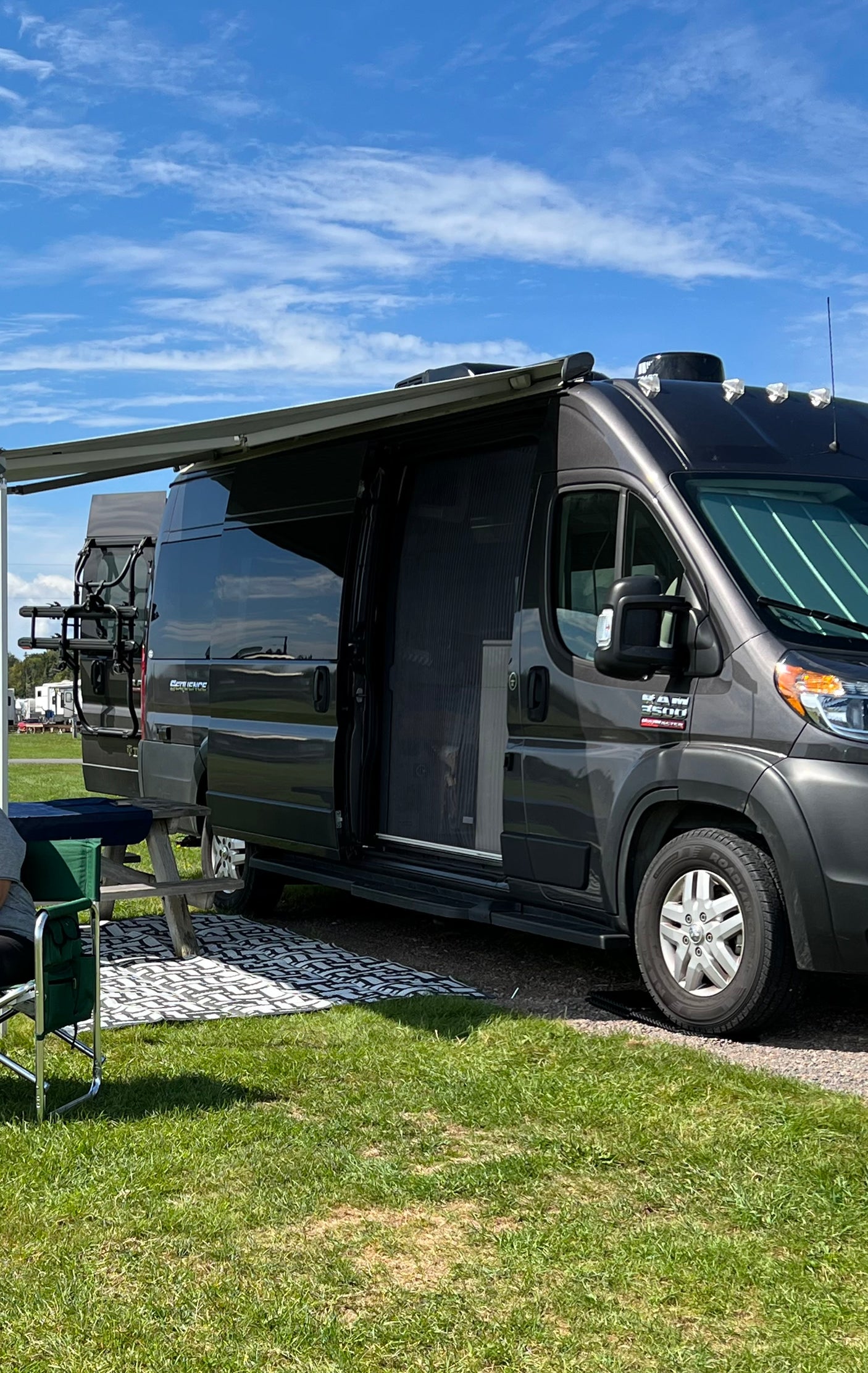 Dark gray RV rental with extended awning and open screen door, parked on grass. Ideal for a summer camping trip.