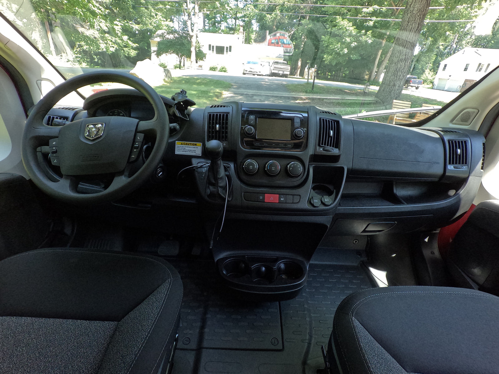 Dashboard and interior of an RV rental, offering a driver's view of the road, houses, and trees through the windshield.