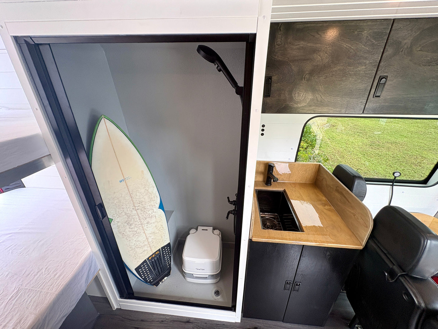 This RV rental showcases a compact interior with a shower, toilet, surfboard, kitchenette, and sleeping area.