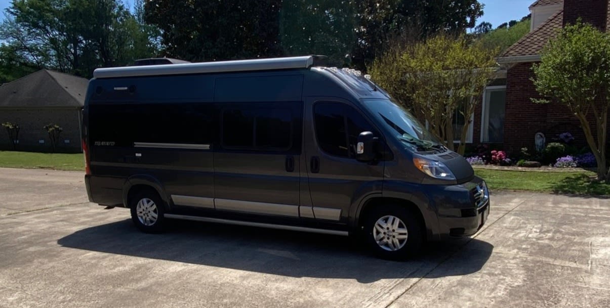 Dark grey camper van (rv rental) with an awning parked on a driveway. A house