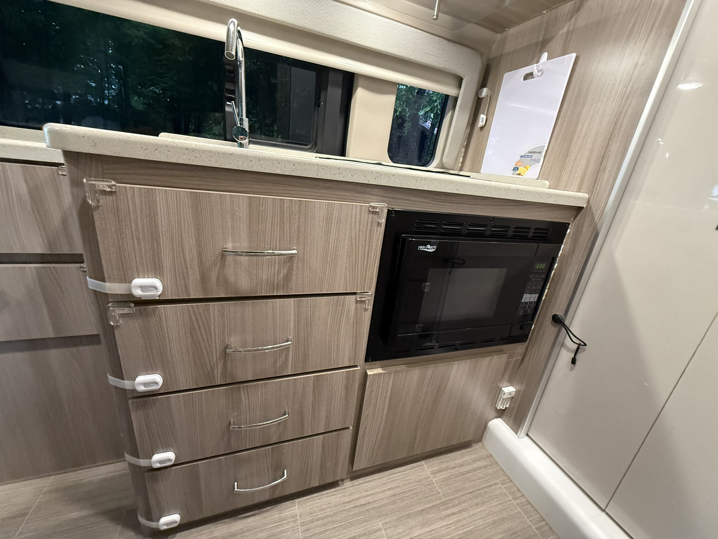 This rv rental features a compact kitchen with a sink, built-in microwave, and child-safe drawers for convenience.