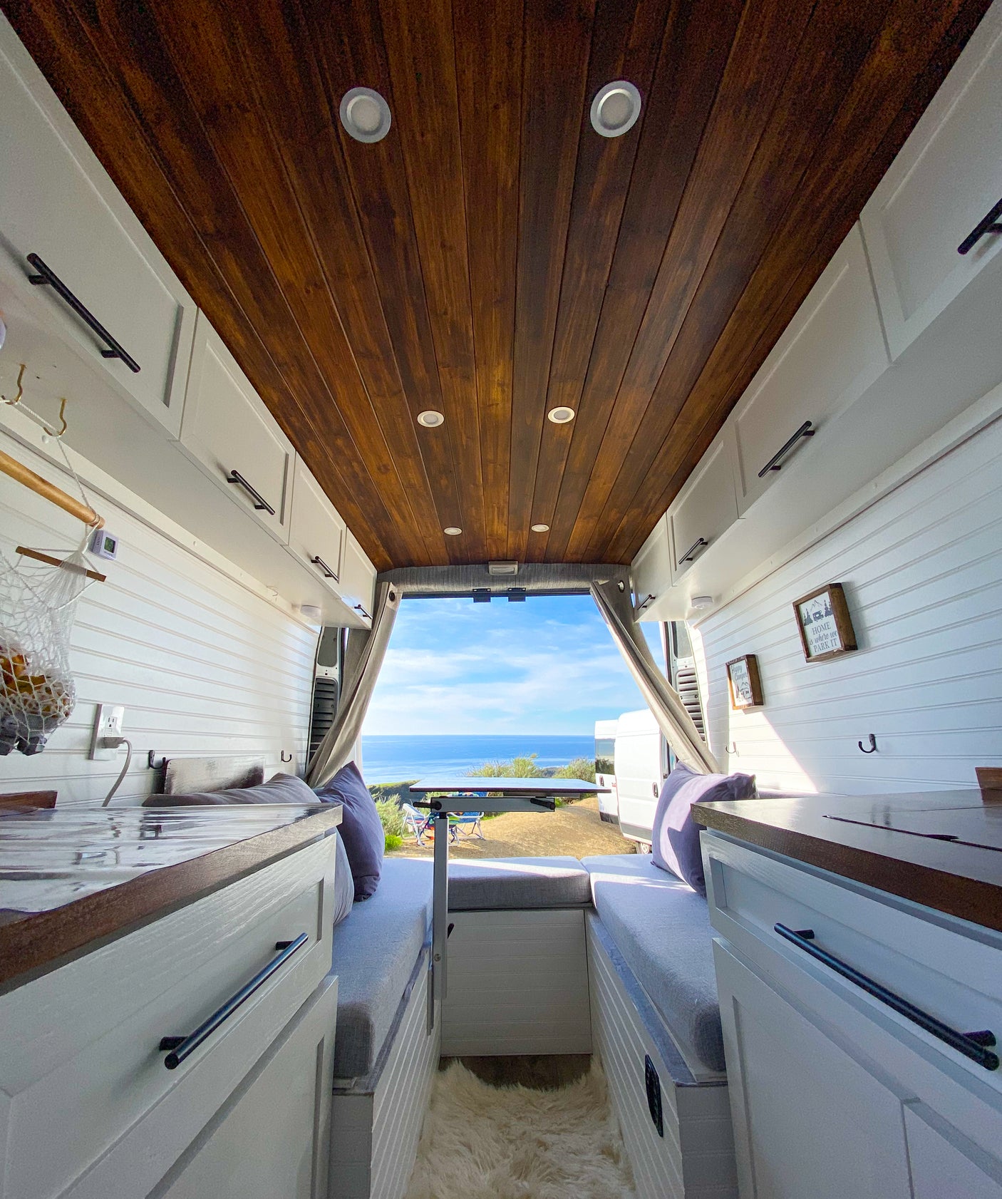 Interior of a modern rv rental camper van, featuring a wooden ceiling, white cabinets, and an ocean view.