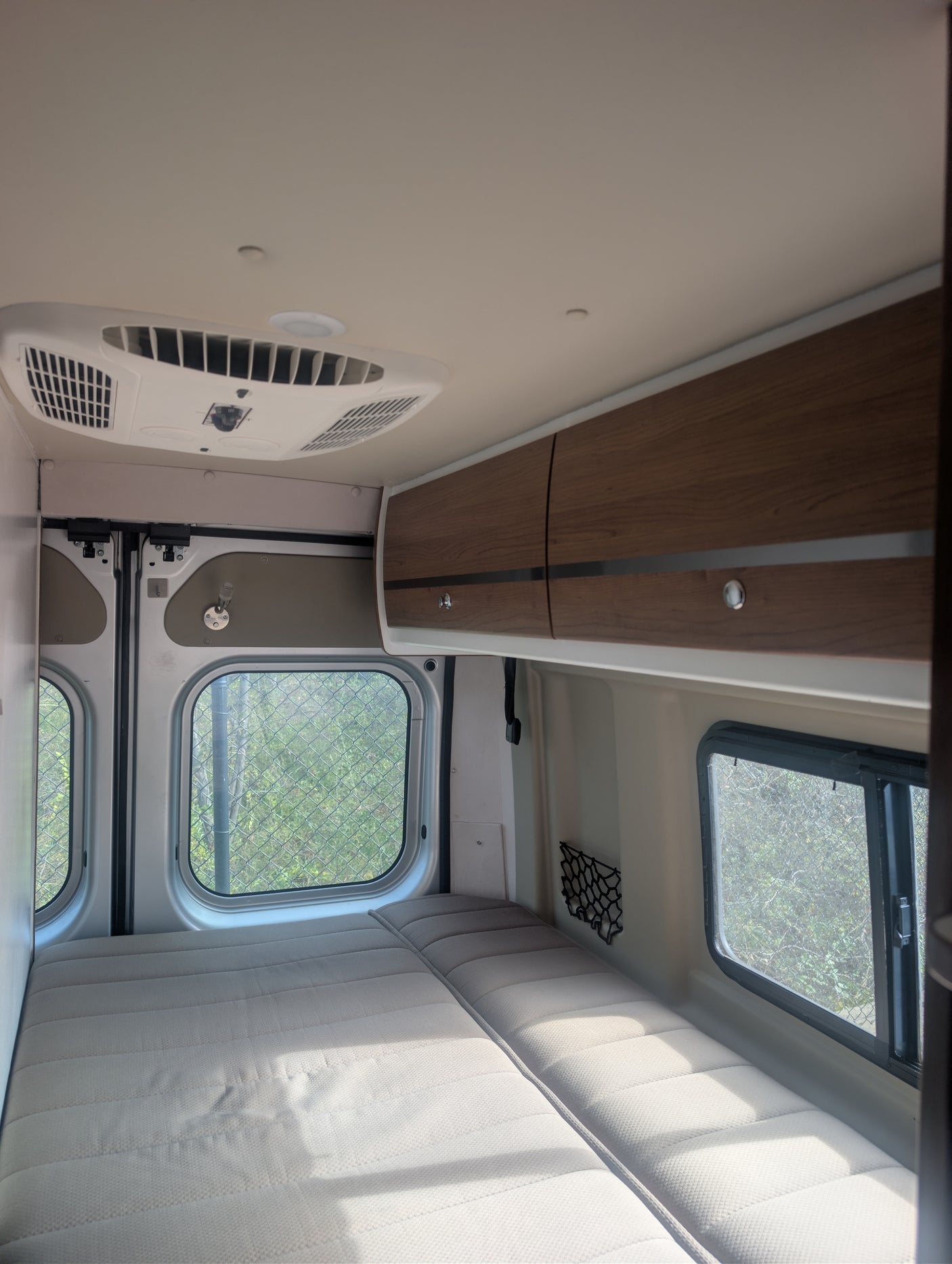 Cozy interior of an RV rental featuring a comfortable bed, windows, overhead cabinets, and an AC unit for your travels.