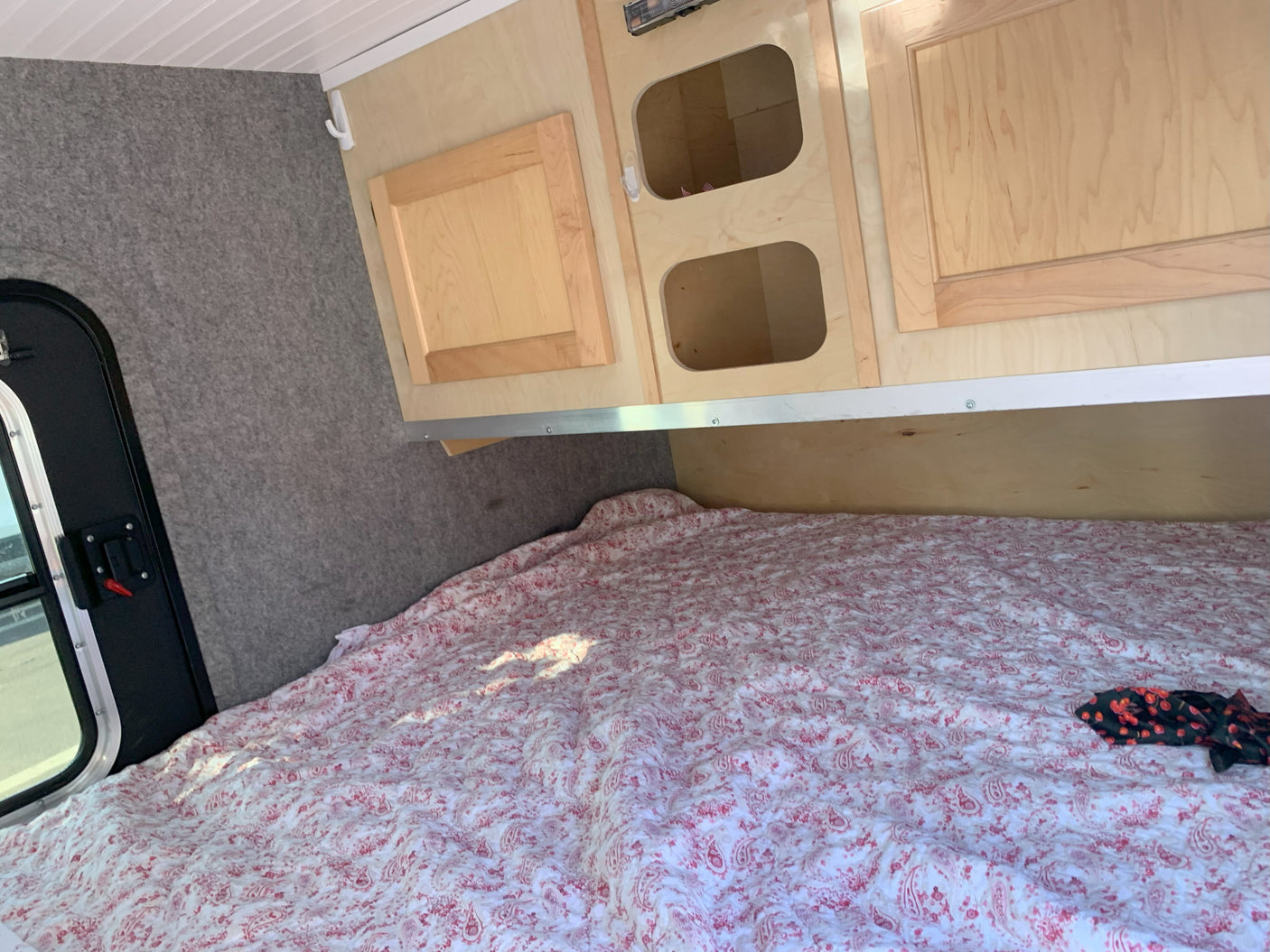 RV rental: Inside a compact camper, showing a red and white paisley bed, wood cabinets, and a side entrance.