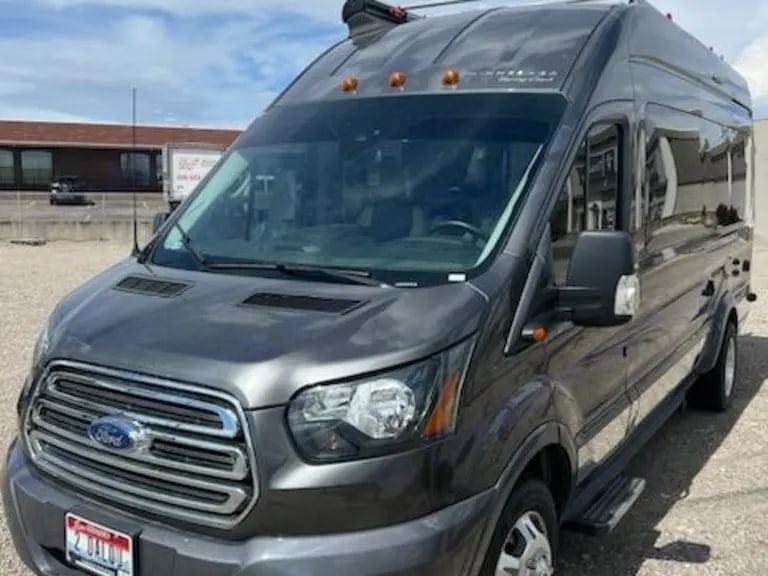 surrounded by trees under a cloudy sky.|A sleek gray Ford Transit van RV rental