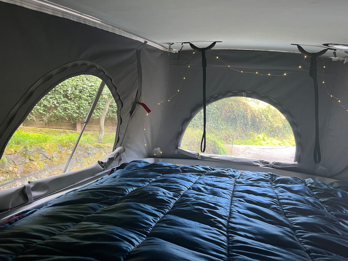 Cozy pop-top RV rental sleeping area with blue bedding, fairy lights, and scenic views. Ideal for camper travel.