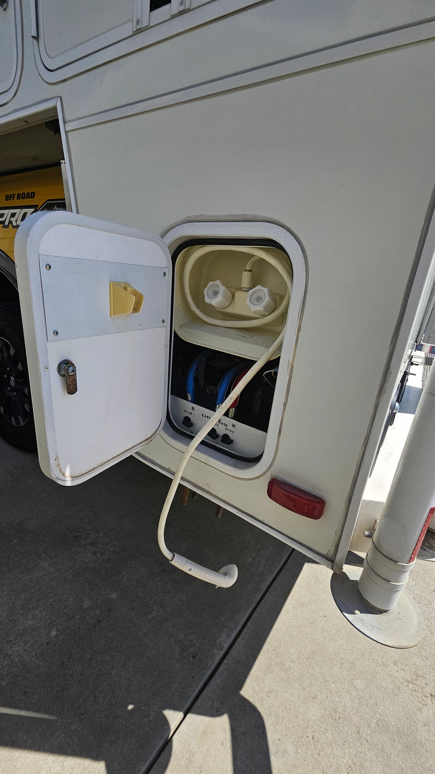 RV rental: Open utility compartment on a white RV, showing an outdoor shower with hose and hot/cold water valves.