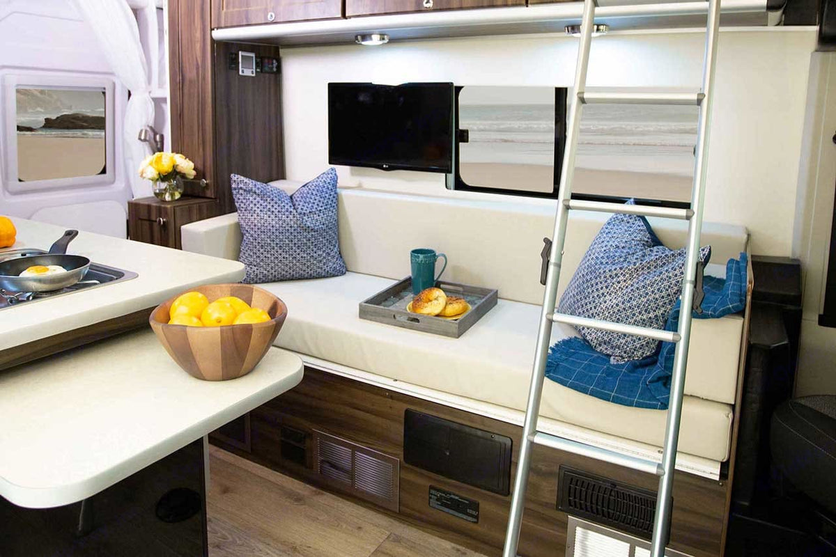 and beach-view window. Ladder indicates sleeping bunks for travel.|Inside a modern RV rental: compact kitchen with stove & fridge — photo 12