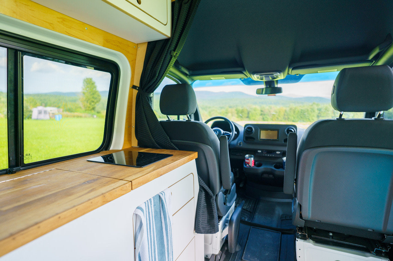 RV rental van's interior: kitchenette, front seats, and scenic outdoor view through windows.