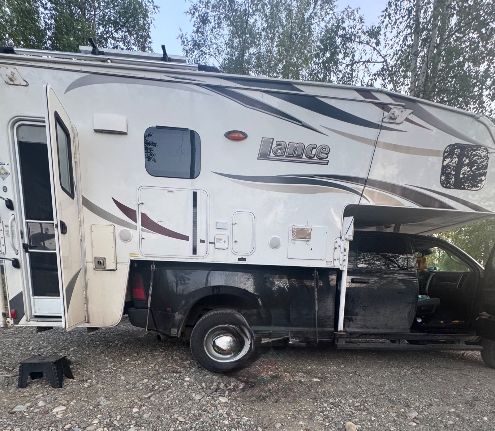 This white Lance truck camper, a type of RV rental, is ready for adventure. Open door & outdoor step visible.