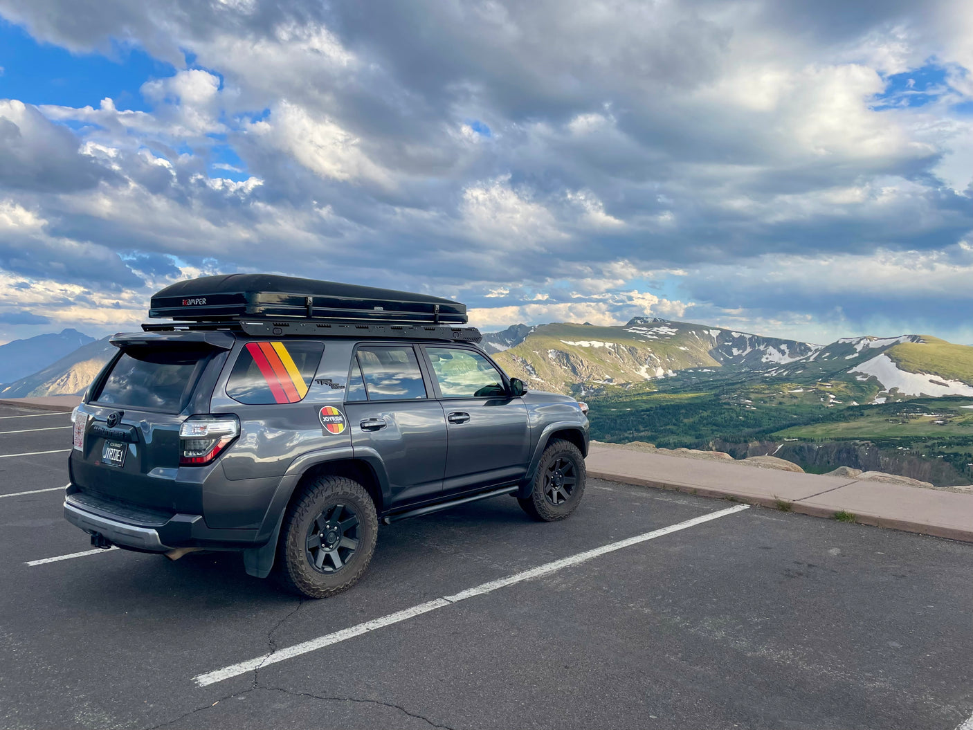 A grey SUV with a rooftop tent sits at a mountain overlook. Ideal for adventure travel; an RV rental can offer similar experiences.