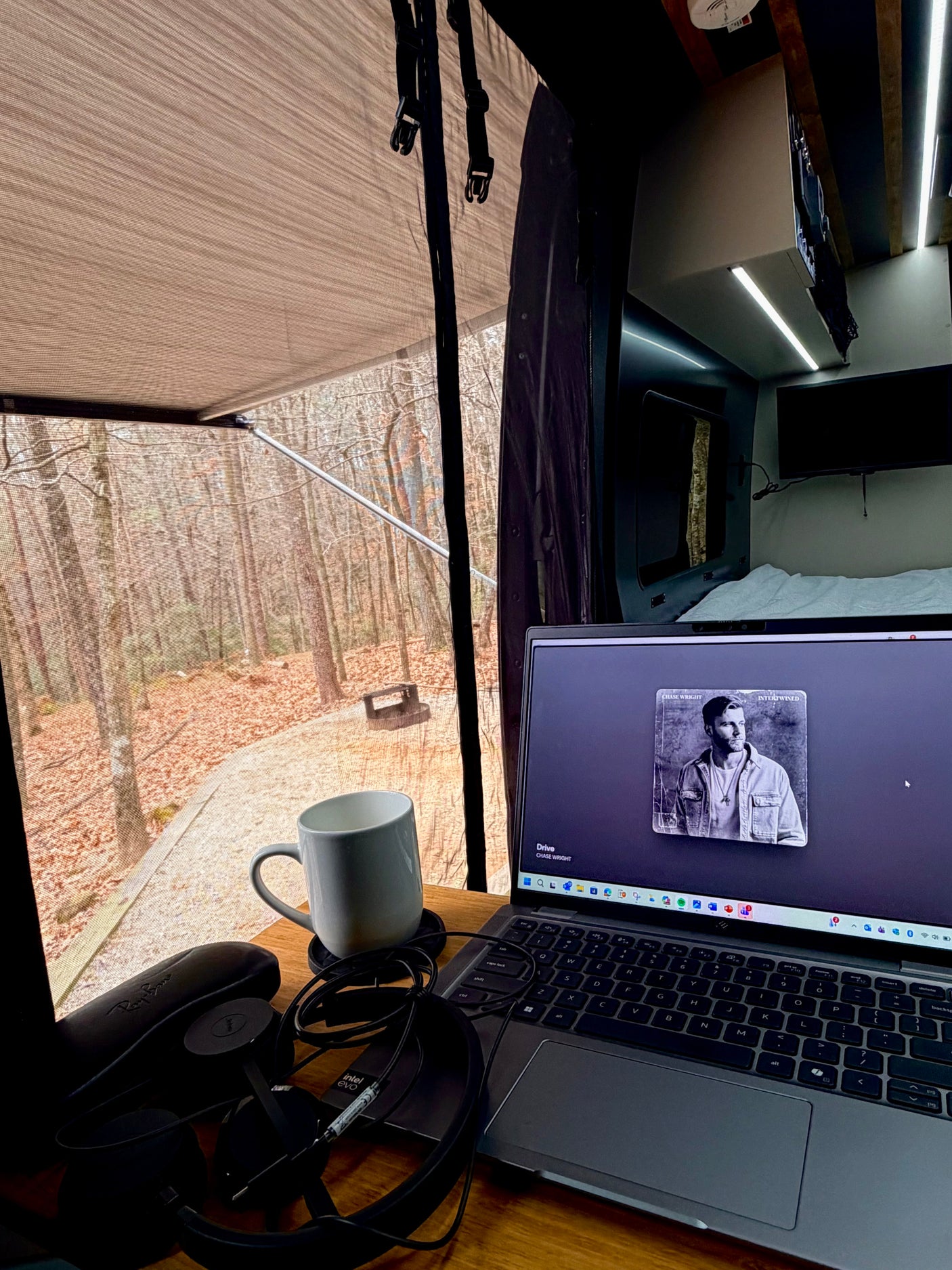 An RV rental offers a perfect mobile workspace: laptop, coffee, headphones, and a tranquil forest view through the screen.