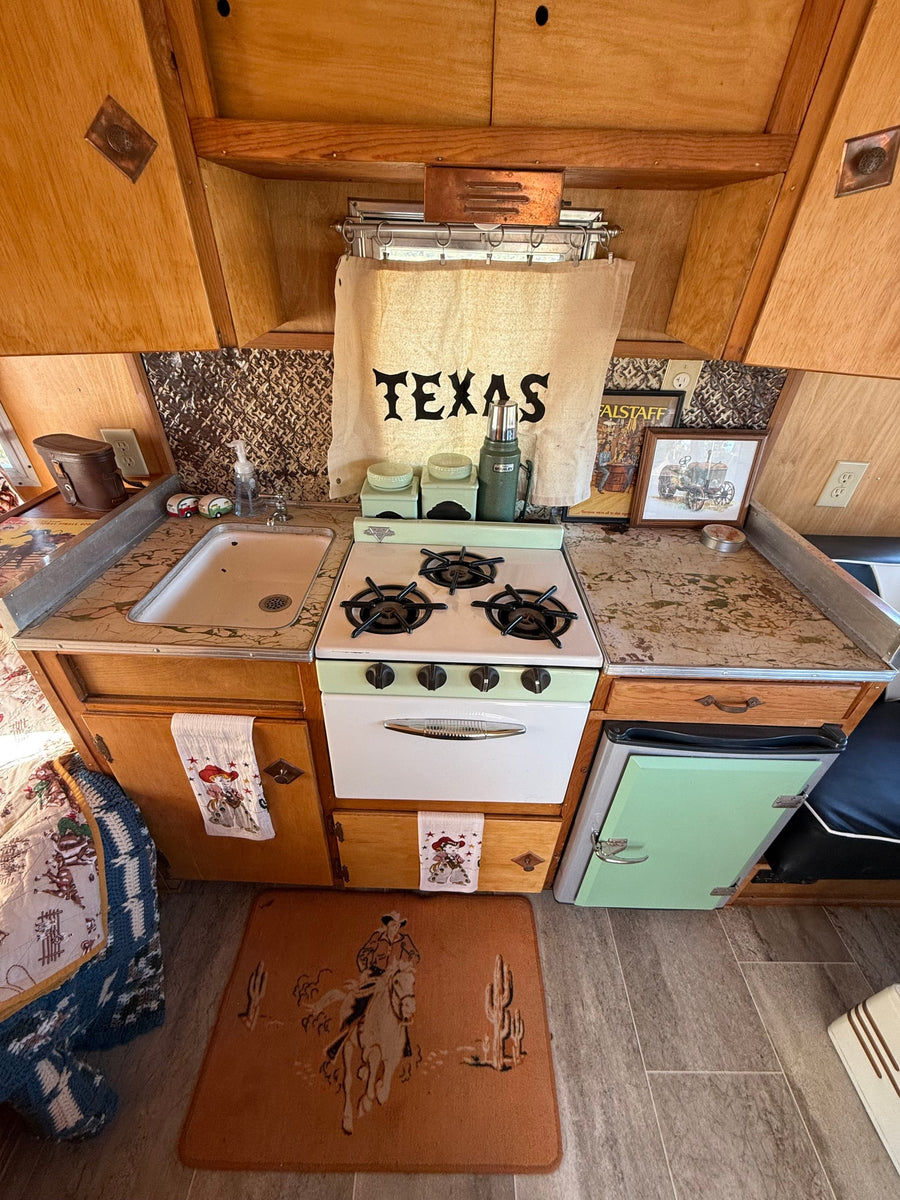 Step inside this charming RV rental kitchen with its mint green stove, sink, and vintage Texas-themed decor. Compact and retro.