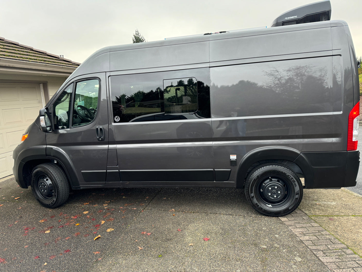 Sleek gray camper van, ideal for RV rental. Side view with windows, roof AC unit, and external electrical connection.