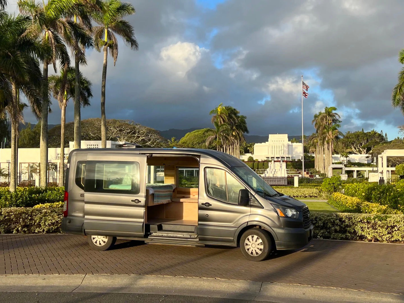 RV rental campervan parked by the Hawaii temple with its side open, showing the cozy wooden interior, under a cloudy sky.