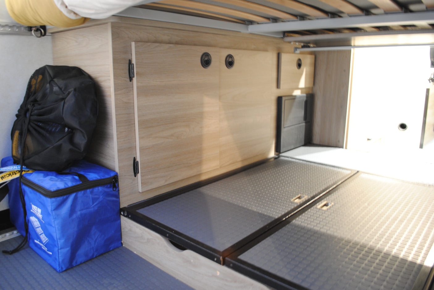RV rental interior: Under-bed storage area with cooler bag and black mesh bag.