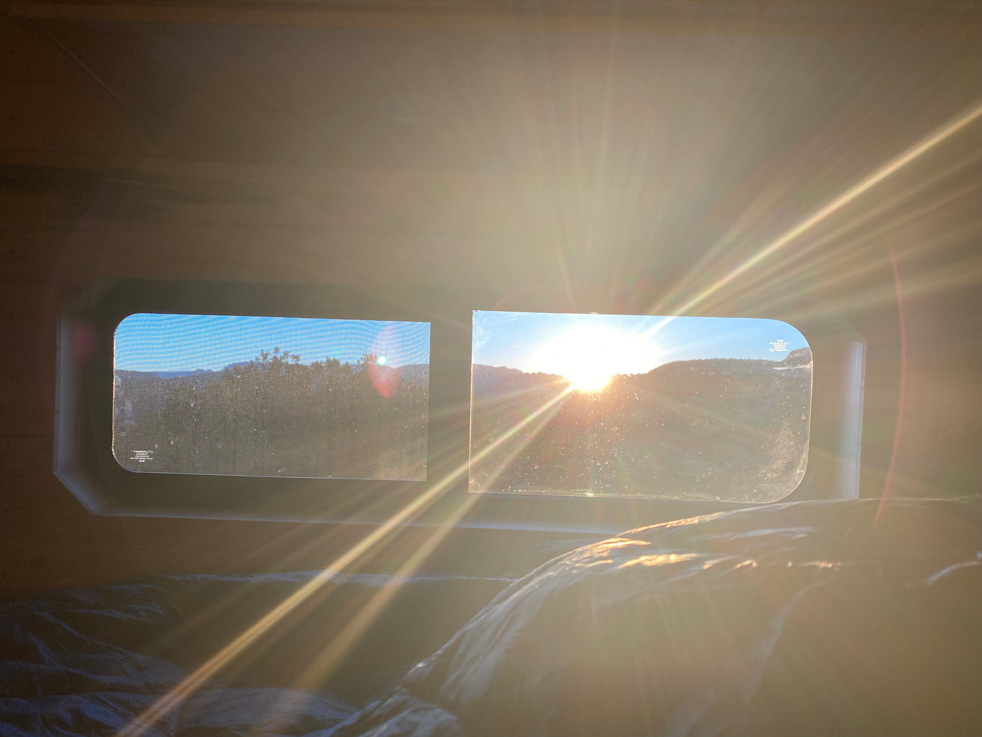 Sunrise from an RV rental, with bright sun rays streaming through screened windows overlooking mountains. Cozy morning view.