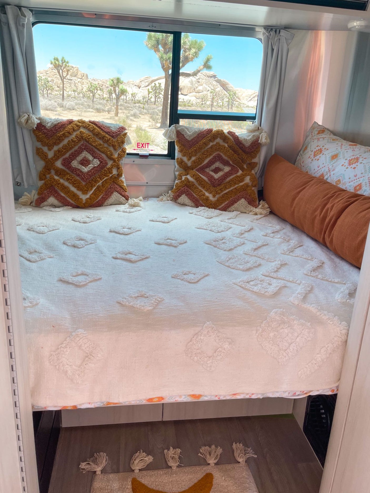 Cozy RV rental bedroom with textured bedding and decorative pillows, offering a stunning Joshua Tree desert view.