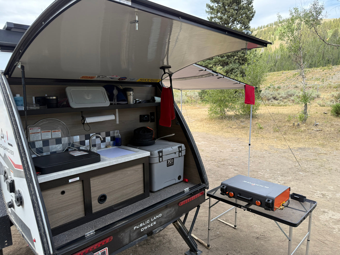 This RV rental's outdoor kitchen features a sink, cooler, and a Blackstone griddle under an awning, perfect for camping.