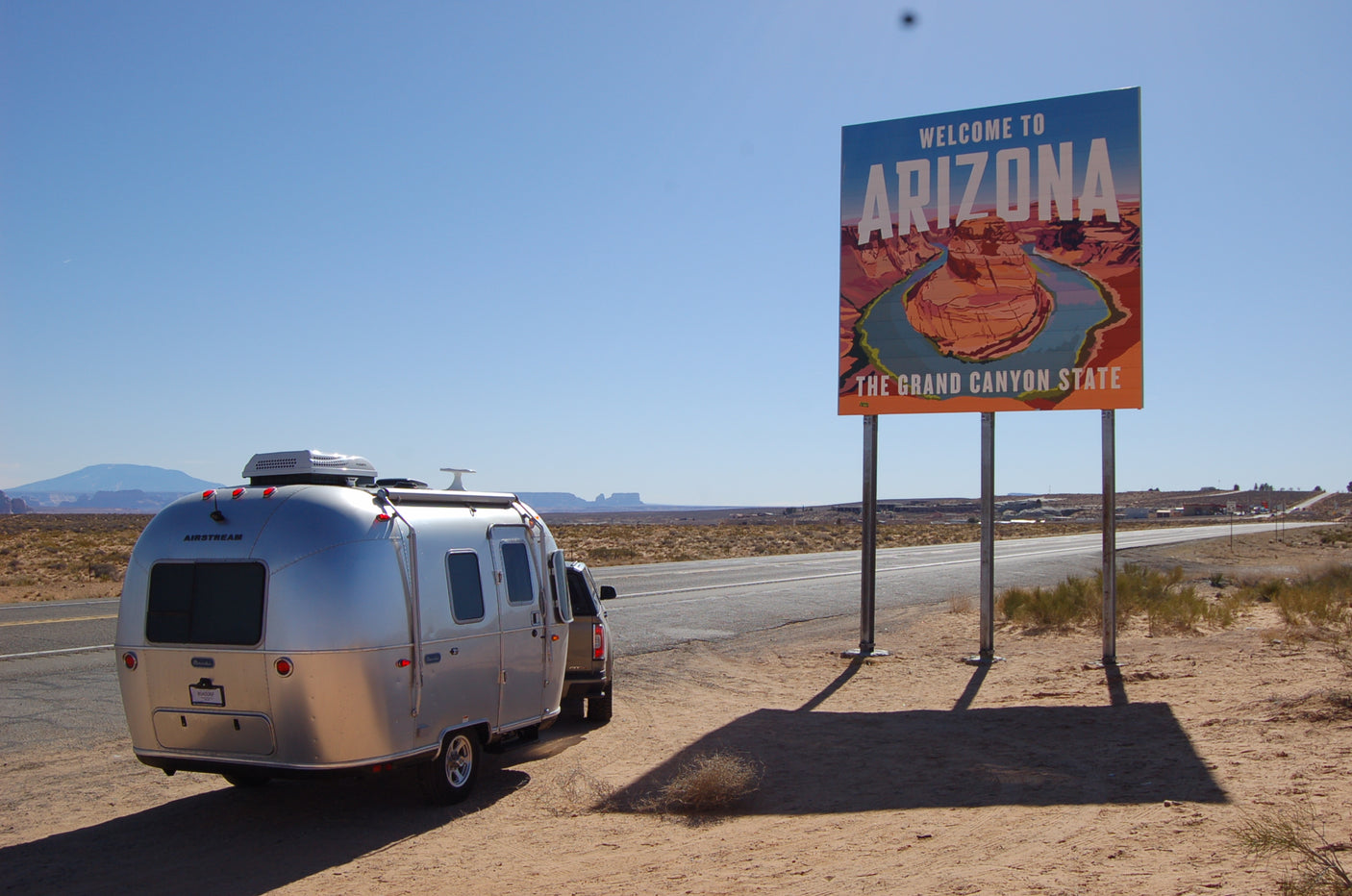 RV rental journey begins! An Airstream trailer next to Arizona's welcome sign on a sunny desert roadside.